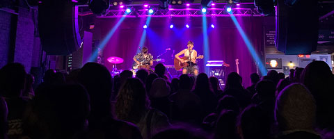 Isa Ansin playing acoustic guitar in a packed concert venue