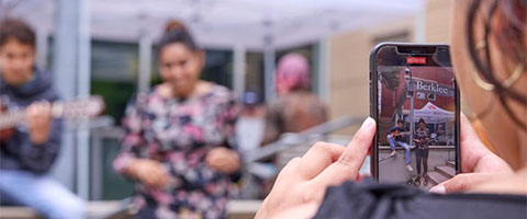 A student uses a phone camera to film a group of student musicians 