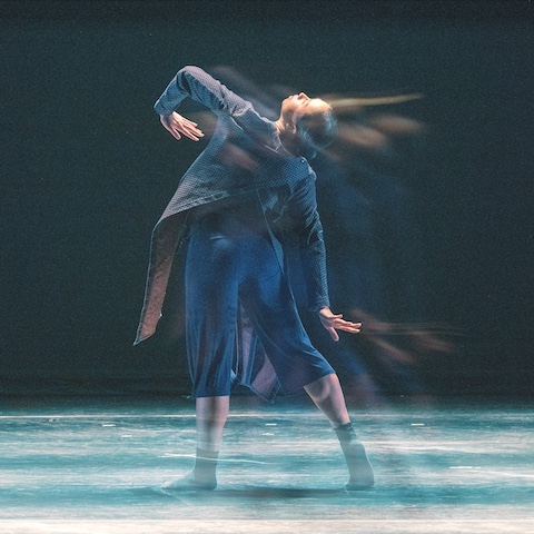 Dancer mid-motion on stage with their head leaned back in a blue/navy shirt and pant set.