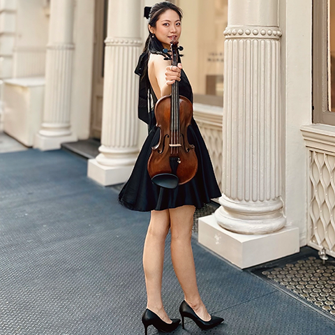 Youngmi Hwang posing with violin in front of columns.