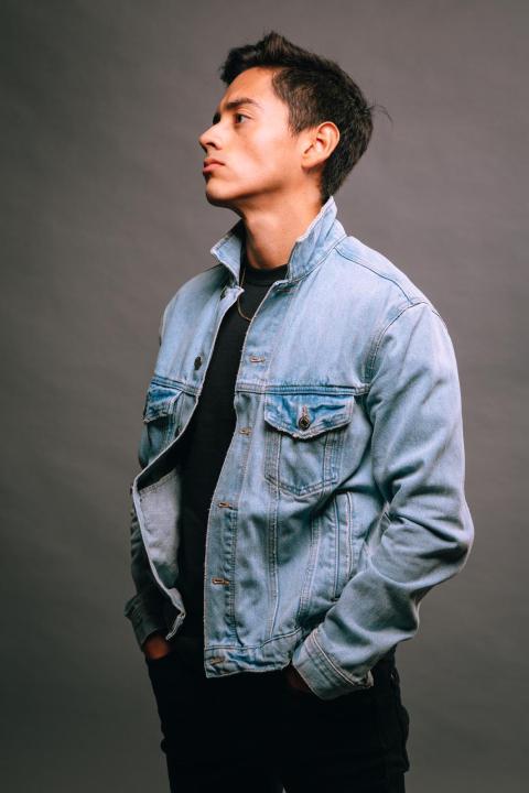 a man in a jean jacket in front of a gray backdrop